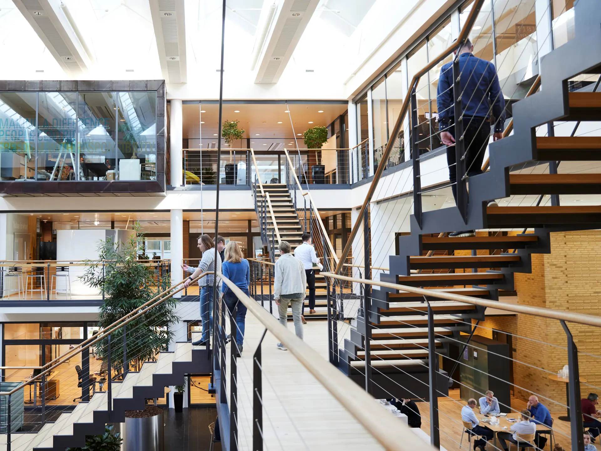  A modern, open-concept stairway inside the Systematic headquarters in Aarhus, with employees walking and collaborating in a bright, spacious office environment